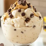 High-protein Ninja Creami ice cream in a bowl, topped with chocolate chips and peanut butter swirl, with a Ninja Creami machine and healthy ingredients in the background