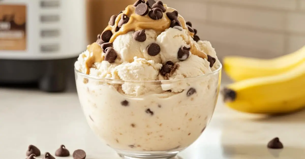 High-protein Ninja Creami ice cream in a bowl, topped with chocolate chips and peanut butter swirl, with a Ninja Creami machine and healthy ingredients in the background