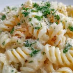 Fusilli pasta coated in creamy garlic parmesan sauce served on a white plate with parsley and grated cheese.