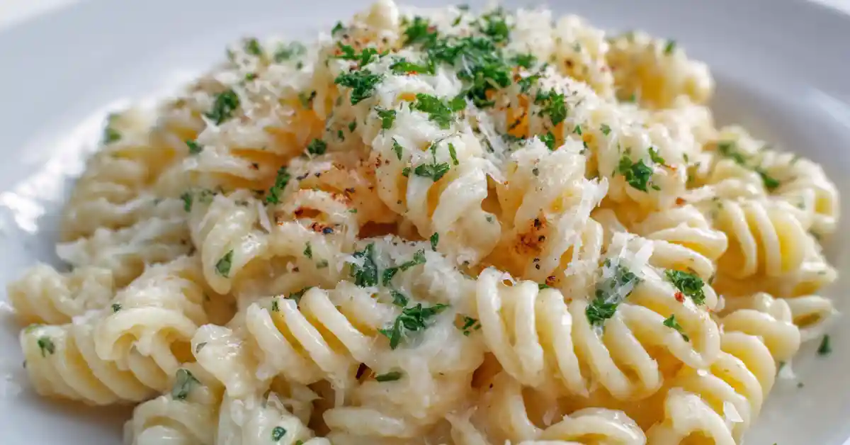 Fusilli pasta coated in creamy garlic parmesan sauce served on a white plate with parsley and grated cheese.